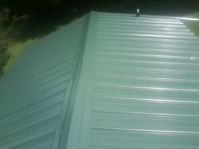 New green metal panels meeting at the ridge of a roof — Flat Roof Repair work by our crew in Monroe
